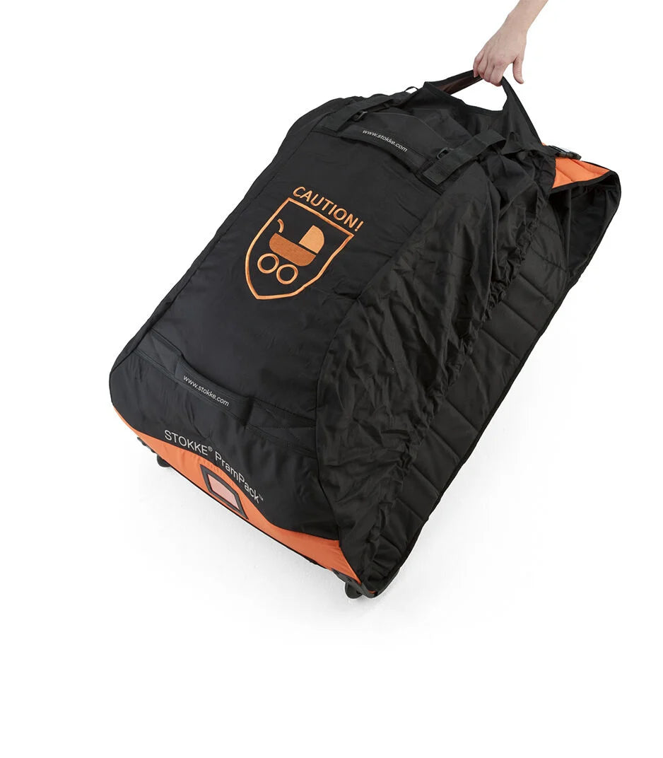 Täyteen pakattu musta-oranssi Stokke PramPack -kuljetuslaukku, jota vedetään kahvasta sen omien pyörien varassa.